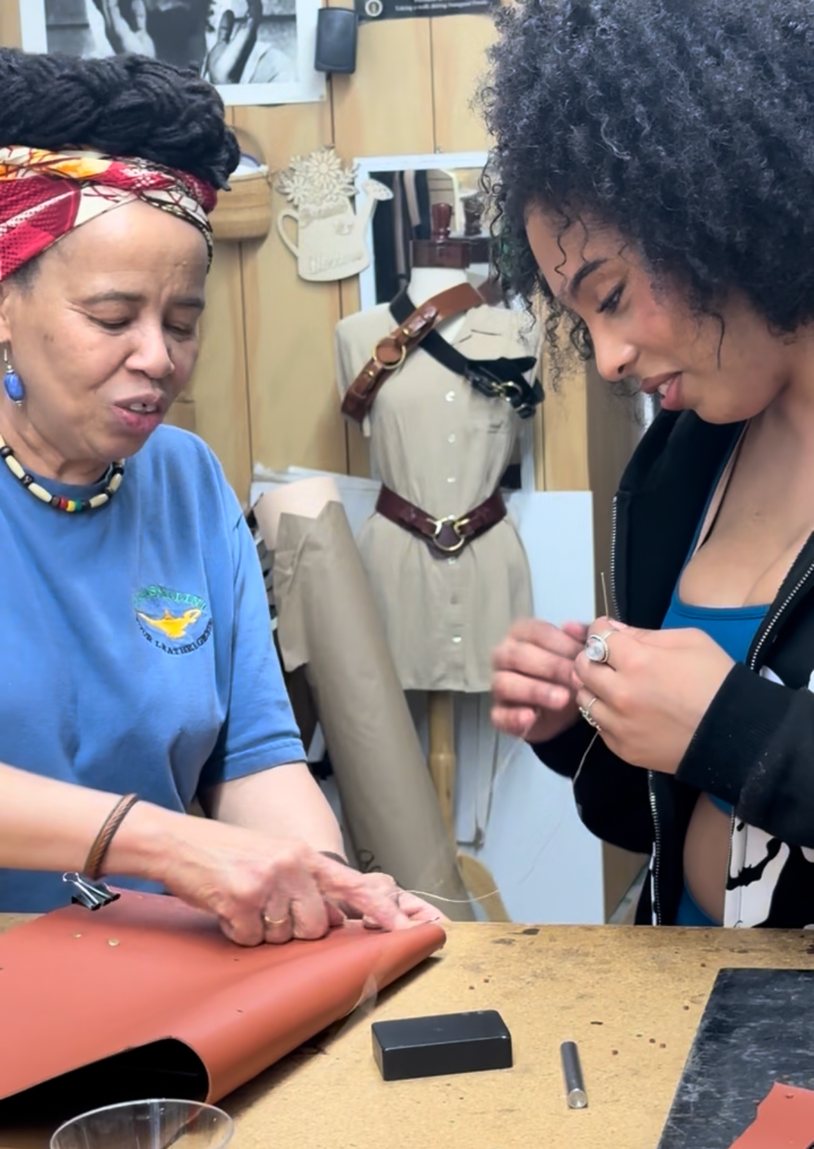 Two women working together in a workshop with leather and sewing materials.